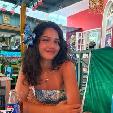 Young woman with flower in hair smiling at a colorful Mexican-themed restaurant.