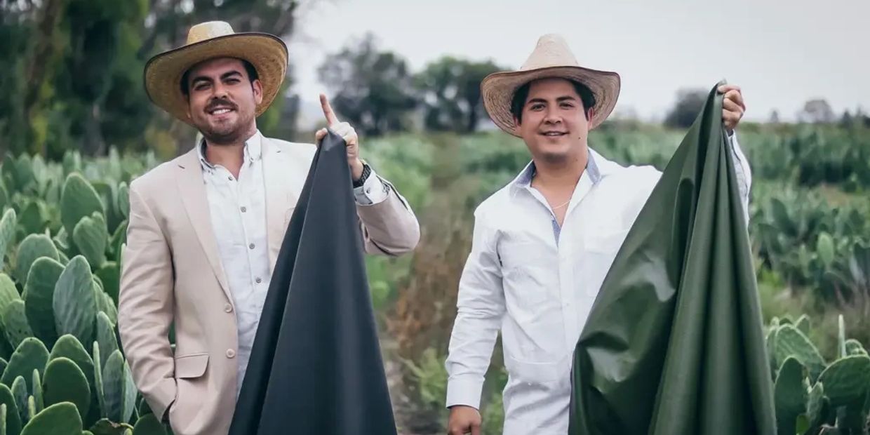 Dos hombres con sombreros sostienen telas en un campo de nopal.