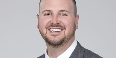 Smiling man in a gray checkered suit and blue tie against a gray background.