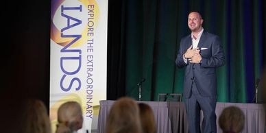 Man in suit speaking on stage at a conference with an audience.