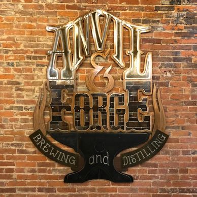 Anvil and Forge Logo in metal mounted on a brick wall.