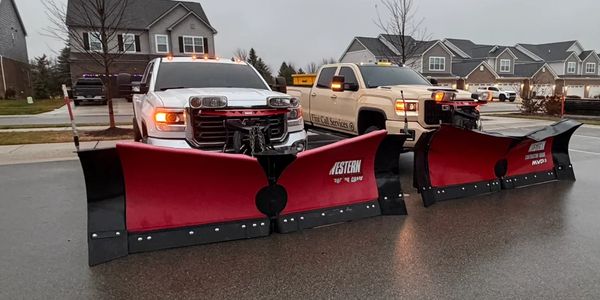 Two trucks with large red snow plows attached.