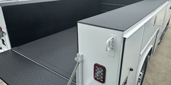 White utility truck with open bed and storage compartments.