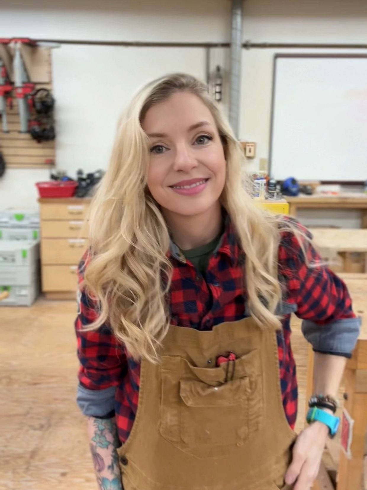 Smiling woman in workshop wearing plaid shirt and apron.