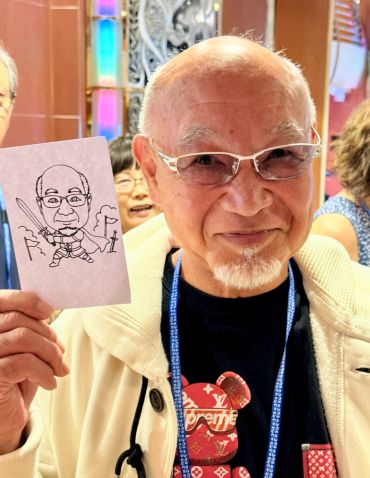 Elderly man smiling and holding a caricature drawing of himself.