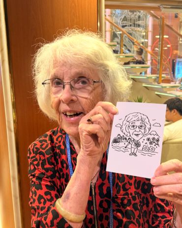 Elderly woman holding a caricature drawing of herself.