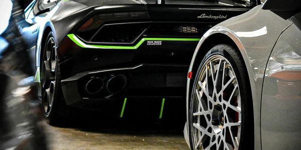 Rear view of a black Lamborghini with green accents beside a silver car wheel.