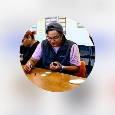 Man writing at a table with others in the background.