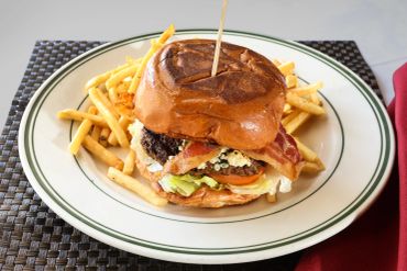 A bacon cheeseburger with fries on a white plate.