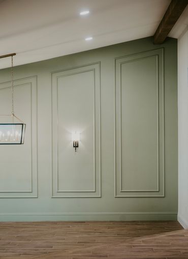 Dining room with sage green paneled walls, wall sconce, vaulted ceiling with decorative ceiling beam