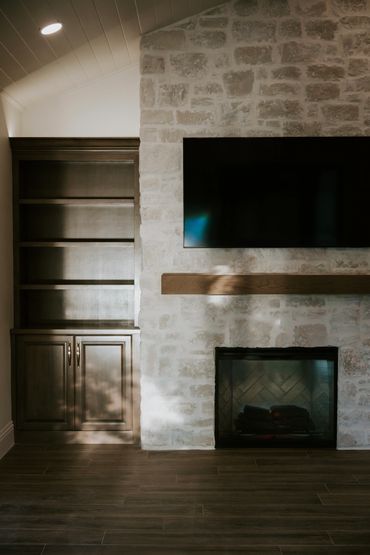 Elegant stone fireplace with custom built-ins on either side, with a white shiplap ceiling above