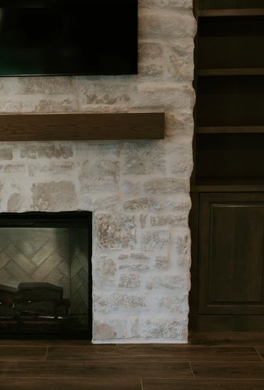 Detailed view of a stone fireplace, rustic wood mantel, herringbone brick firebox, wood cabinetry.
