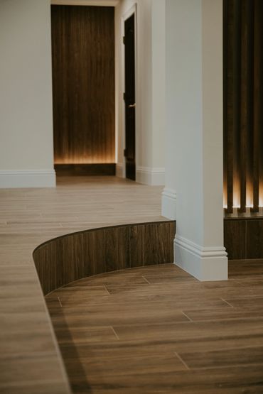 Curved wooden step leading to a sunken living room, with vertical slat wall illuminated at its base
