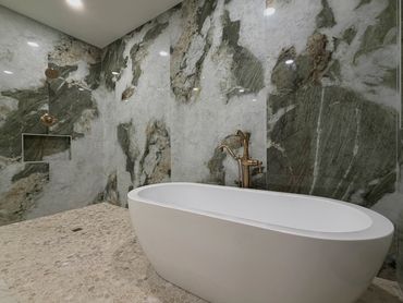 A luxury bathroom with a freestanding tub against dramatic marble slabs with green and gray veining.