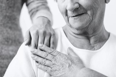 Seated woman touching caregiver's hand with gratitude. Caregiver's hand rests on woman's shoulder.