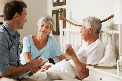 Hospice resident sitting up in bed comfortably with wife and medical professional at his side