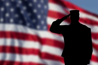 Sillouhette of soldier saluting with U.S. flag waving as the backdrop. Image represents Veteran Aid