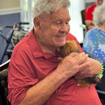 Photo of male resident holding a tiny brown puppy to up to his neck during puppy yogo.