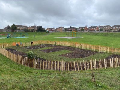 Community garden plots fenced with wooden stakes in a neighborhood park.