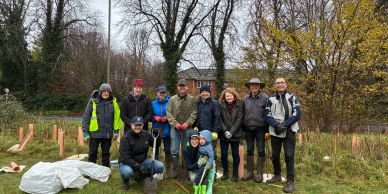 Group of people posing outdoors on a cloudy day with gardening tools.
