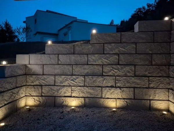 Outdoor stone wall with ground lights at dusk.