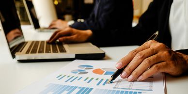 Close-up of hands analyzing charts and using laptops in a business meeting.