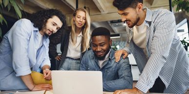 A diverse group collaborates around a laptop in a modern office.