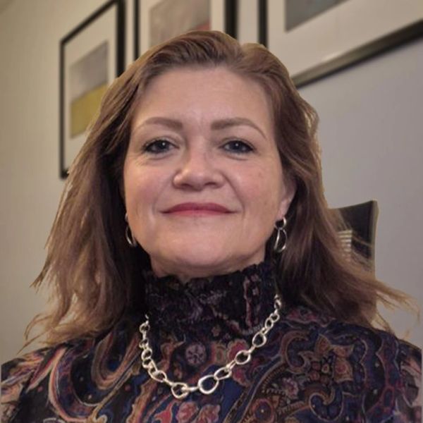 Middle-aged woman with patterned blouse and silver necklace smiling.