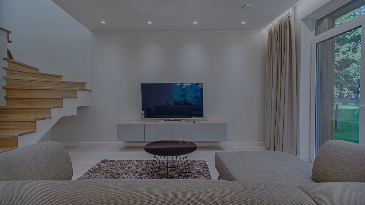 Darkened image of a modern living room with minimal furniture right is glass door, left is staircase