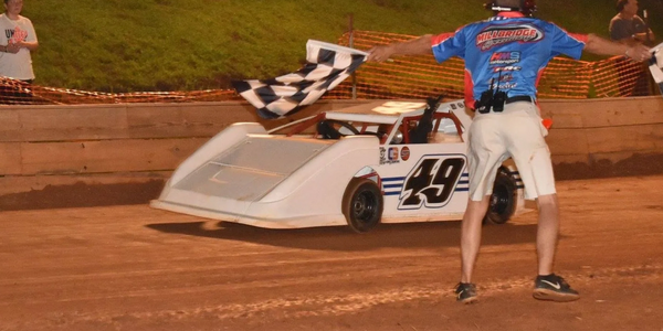 Race car number 49 crosses finish line with flagger signaling.