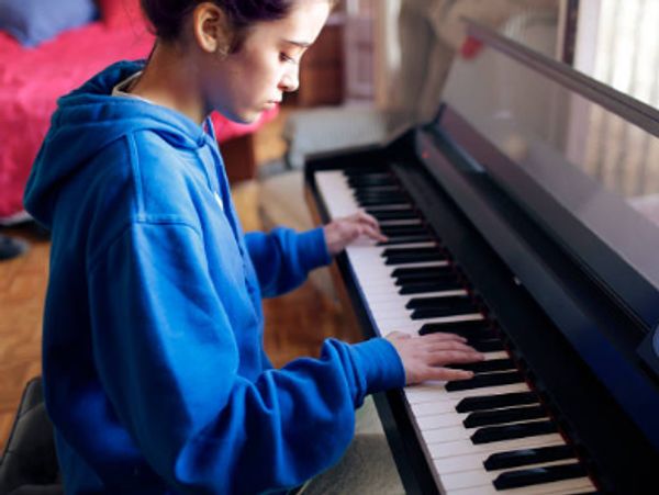 A young person in a blue hoodie playing a piano indoors.