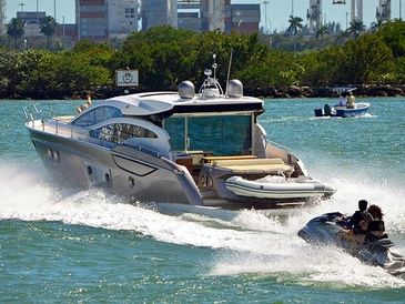 Luxury yacht speeding across the water with jet skis nearby.