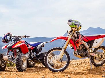 A dirt bike and an ATV parked on a rocky terrain with mountains in the background.