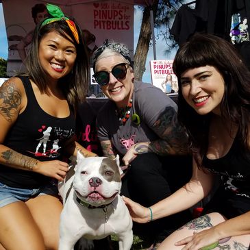 Three smiling women posing with a friendly pitbull at an outdoor event.