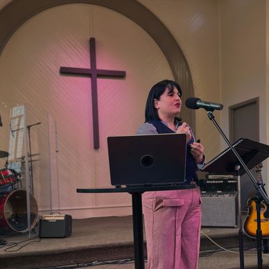 Woman speaking into microphone in church with cross behind her.
