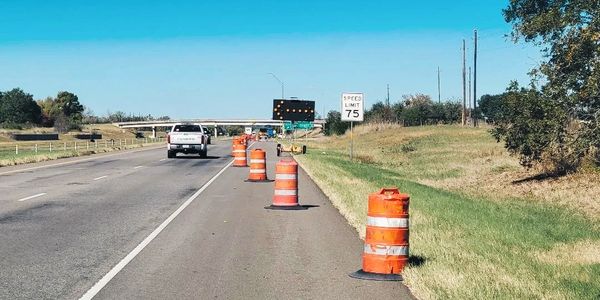 Highway with orange traffic barrels and a speed limit sign of 75 mph.
