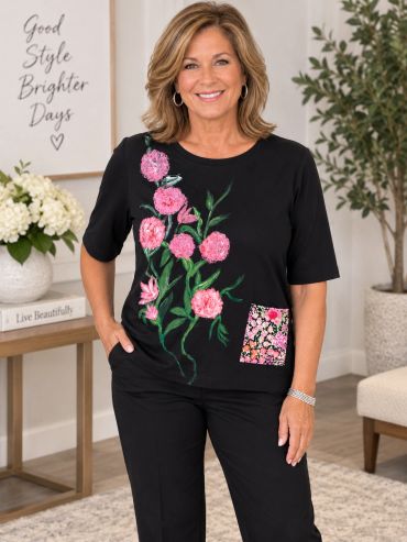 Woman in black outfit with pink floral design smiling indoors.