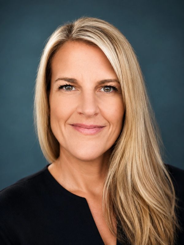 Smiling blonde woman with long hair against a blue background.