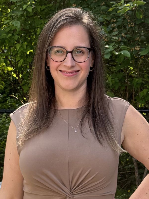 Smiling woman with glasses in a beige top outdoors.