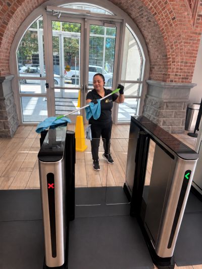 Woman cleaning a glass barrier in a building entrance.