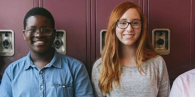 Two smiling students standing in front of school lockers.