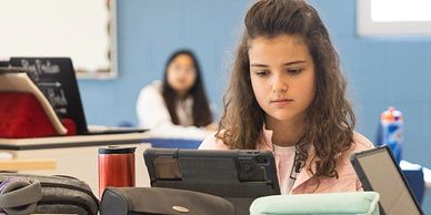 A focused girl using a tablet in a classroom.