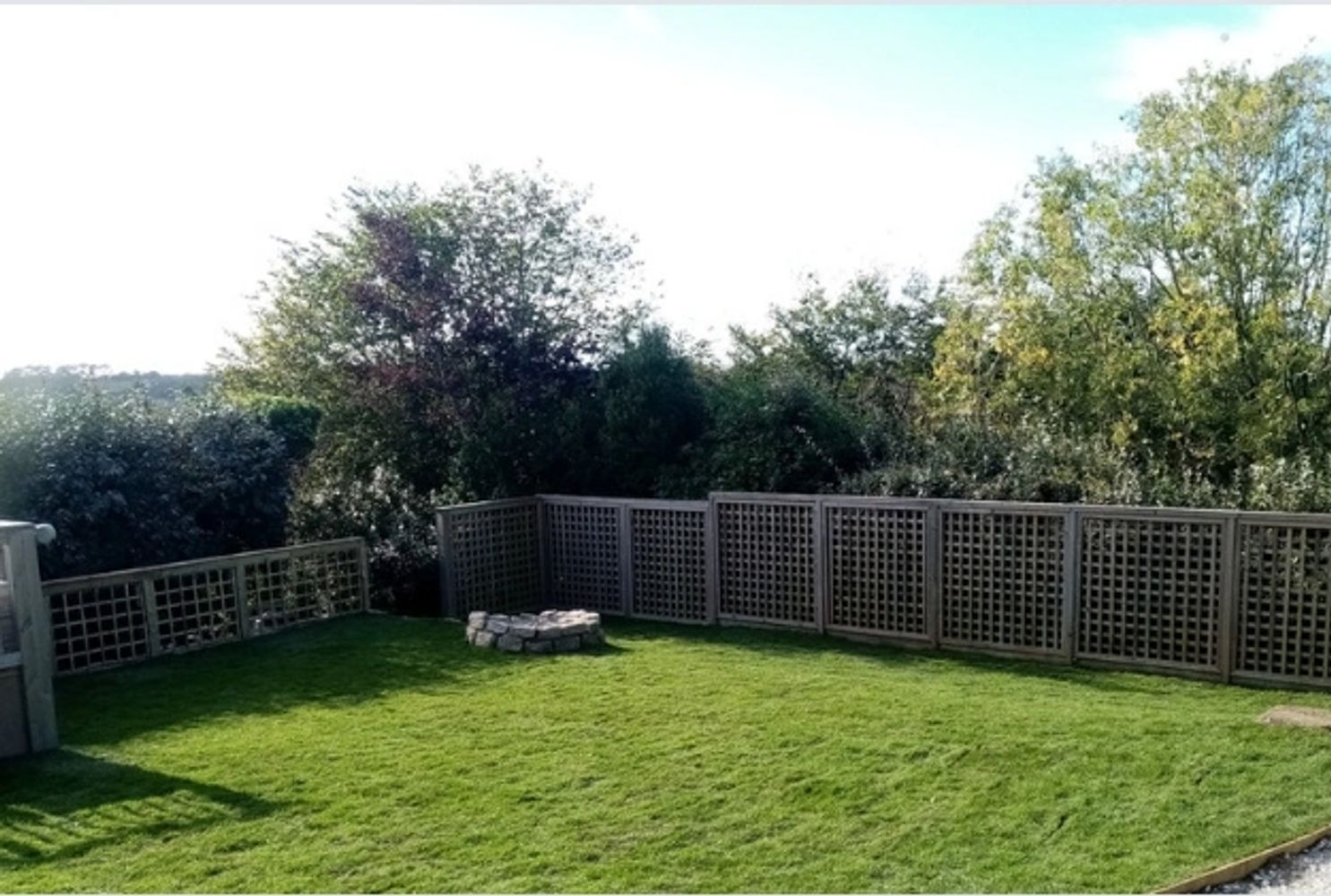 Backyard with green lawn, wooden lattice fence, and a stone fire pit.