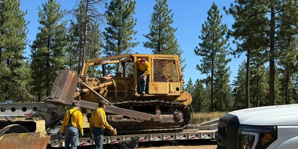 logging equipment with loggers loading it on a trailer for transportation