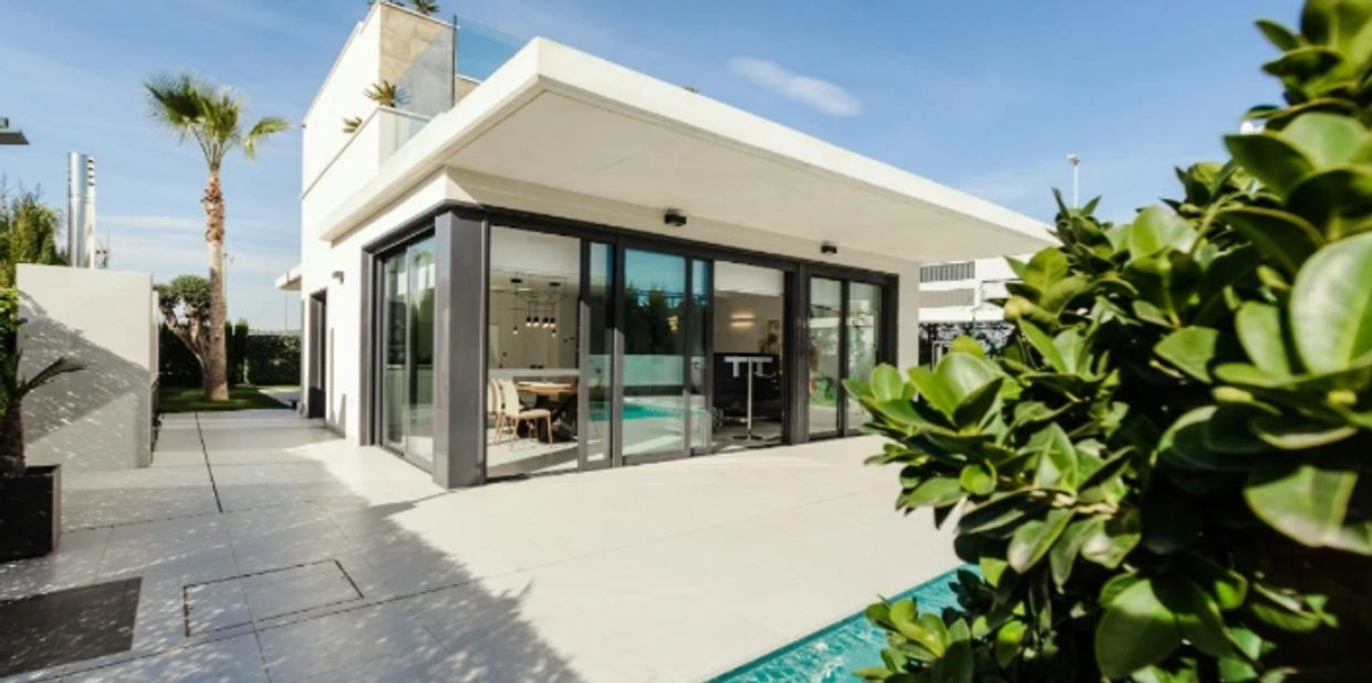 Modern house with glass walls and a pool under a clear sky.