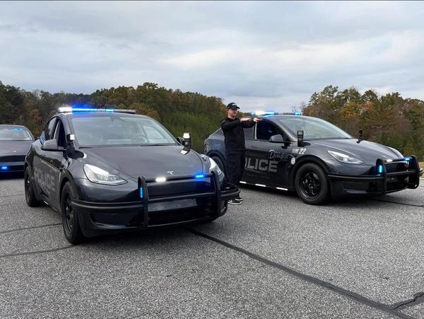 Two black Tesla police cars and one Tesla sedan with blue lights, officer pointing a gun.
