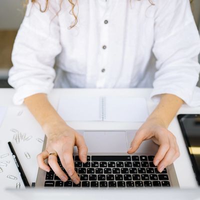 Person typing on a laptop keyboard at a white desk with a notebook and paper clips.
