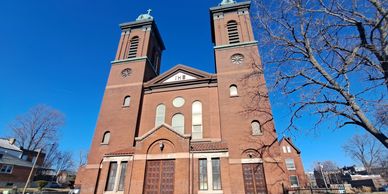 Front view of a large brick church with twin towers under a clear blue sky.
