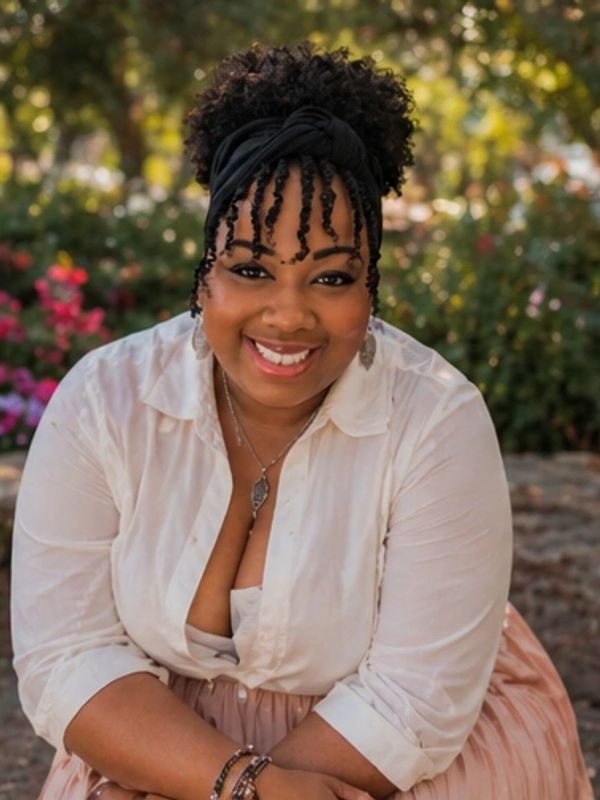 Smiling woman with curly hair and white blouse outdoors.