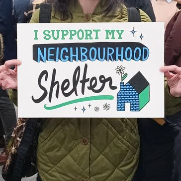 A person holds a sign that reads, "I Support My Neighbourhood Shelter."